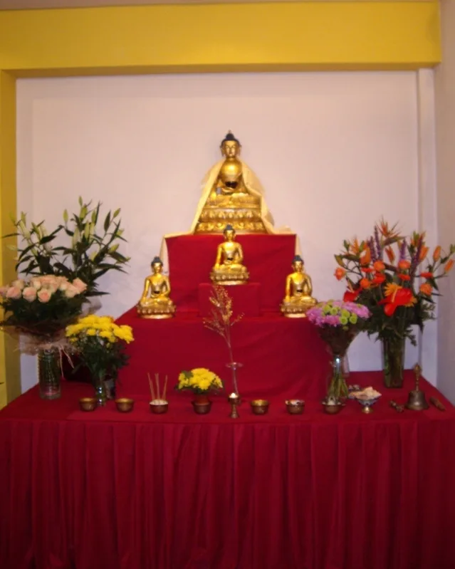 Altar de la gompa de Karma Samten Ling: la figura dorada del Buda sobre un paño rojo, rodeada de figuras menores, flores y ofrendas