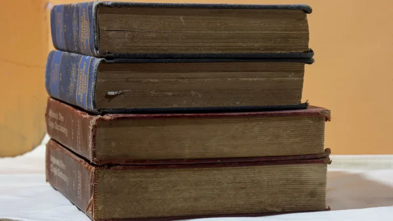 Pila de cuatro libros antiguos de tapas gastadas sobre una mesa, ante una pared ocre