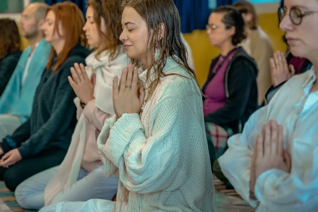 Mujer sonriente con los ojos cerrados y las manos juntas, en fila con otras personas durante una meditación en grupo