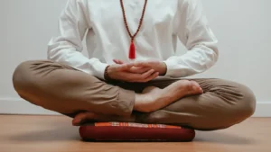 Persona sentada con las piernas cruzadas sobre un cojín de meditación, con las manos recogidas en el regazo